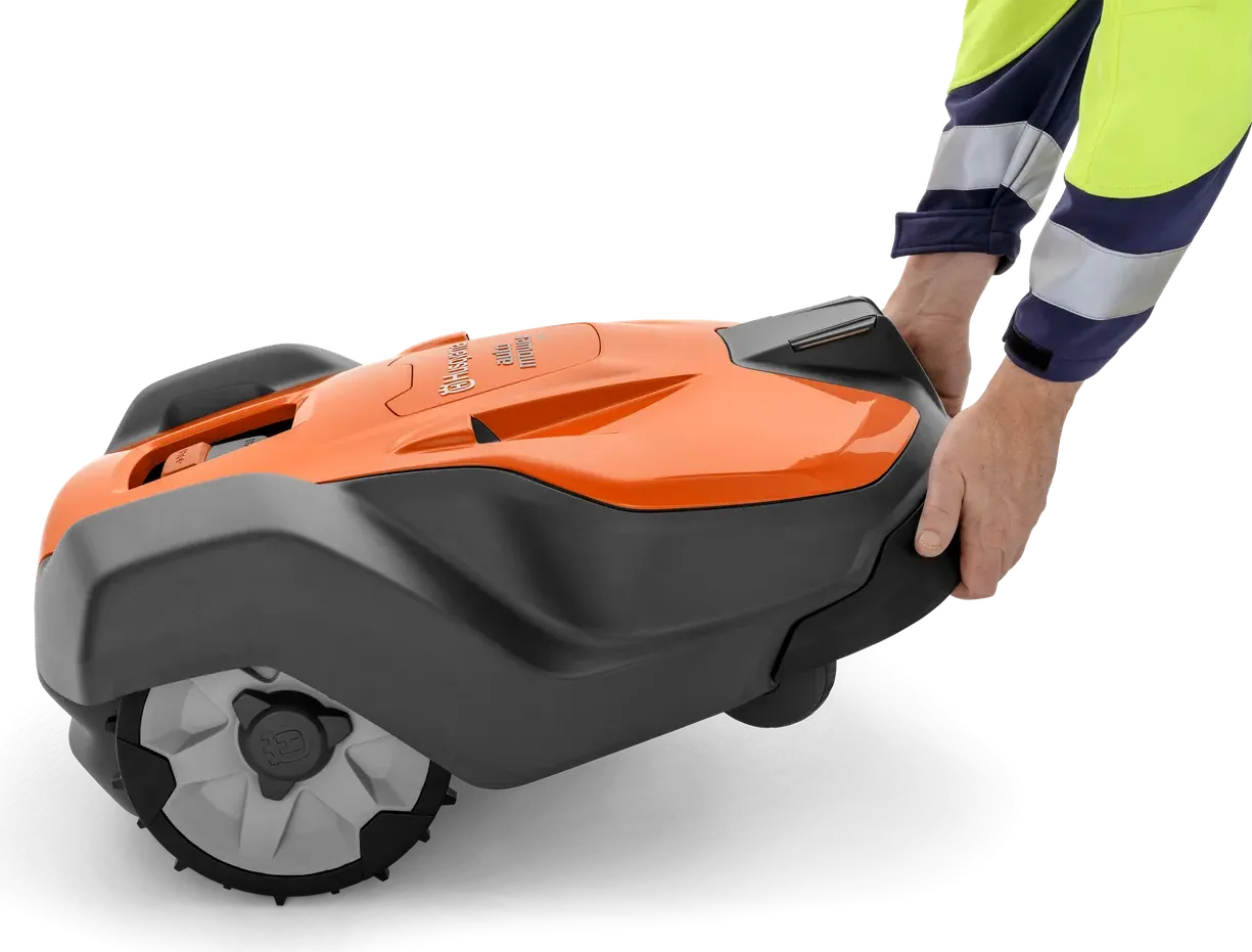 Людина, яка тримає в руках роботизовану газонокосарку Husqvarna, демонструє її конструкцію.