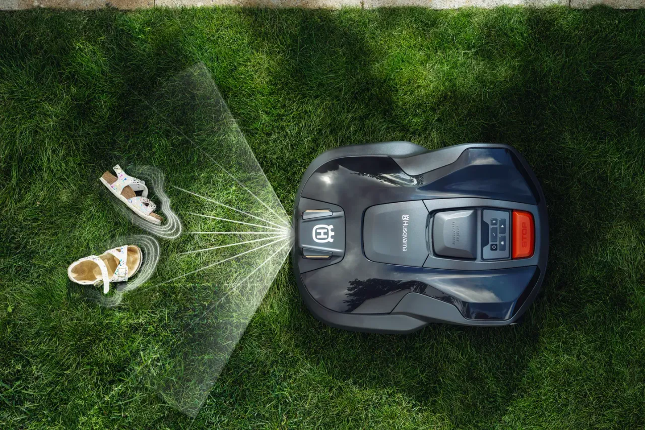 Robotic lawn mower operating on a well-maintained lawn with a pair of sandals nearby.