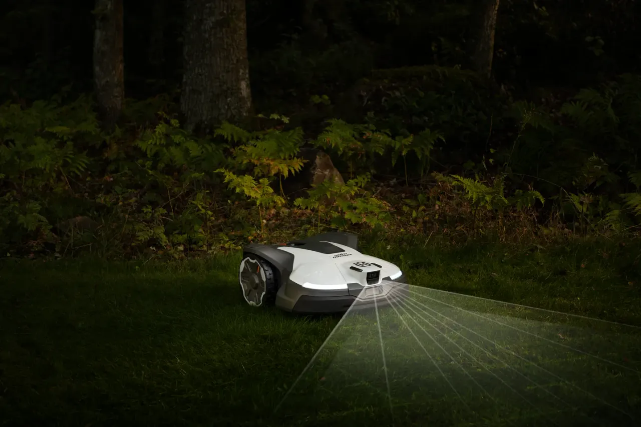 Robotic lawn mower operating in a dimly lit garden with laser guidance lines visible.