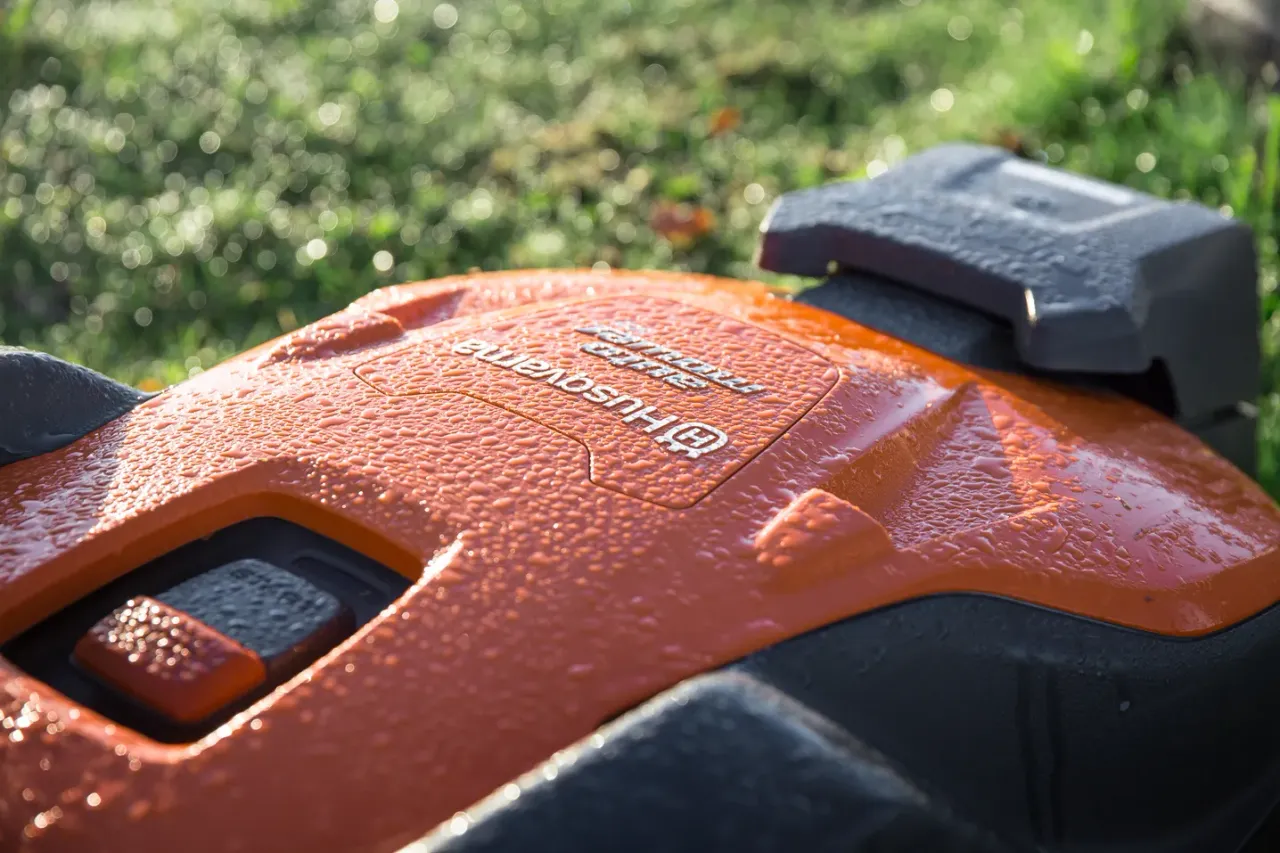 Знімок роботизованої газонокосарки Husqvarna крупним планом із ранковою росою на поверхні.